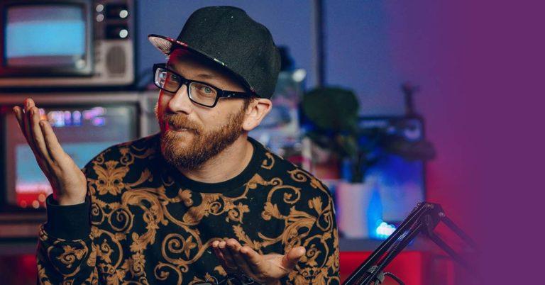 TQS web development: Tyler, a bearded man wearing glasses, a dark cap, and a Bill Cosby-style sweater, gives sideways glance into the camera in his home studio.