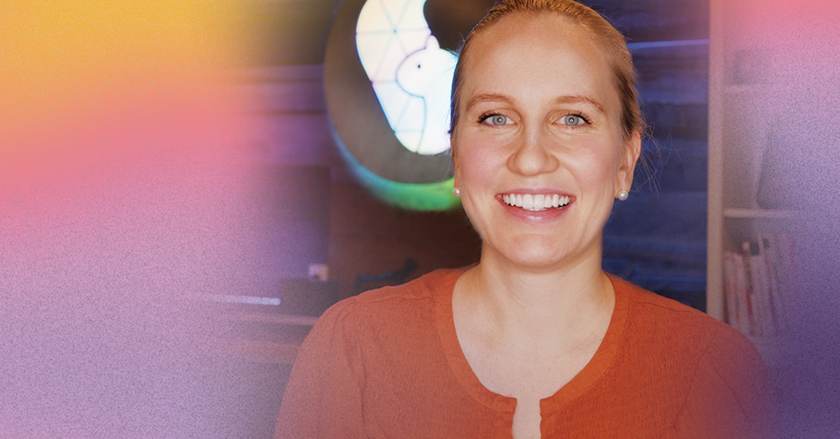 Lisa, a young woman with blonde hair and blue eyes. wears an orange sweater while smiling happily into the camera.