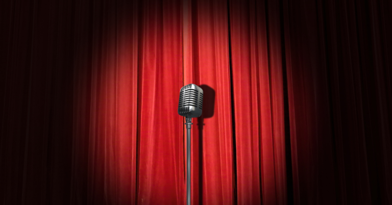 TQS takes on comedy: A microphone stands in a spotlight in front of a red curtain