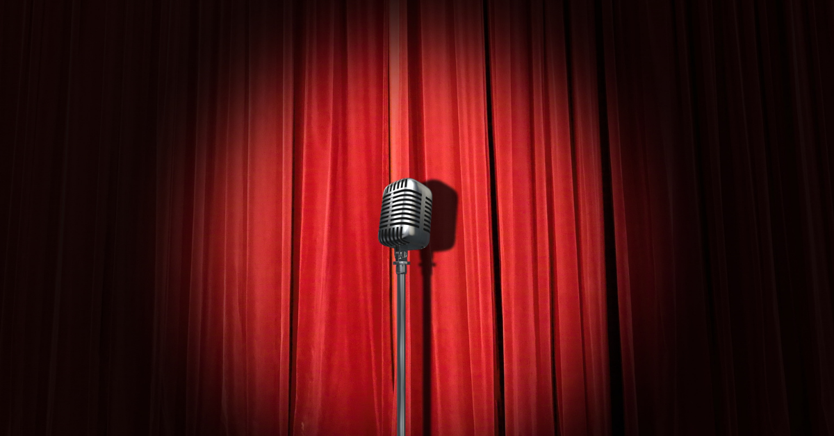 TQS takes on comedy: A microphone stands in a spotlight in front of a red curtain