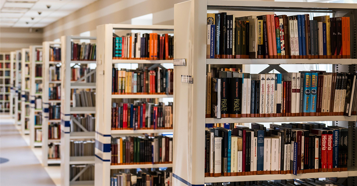 TQS takes on school: A well-lit library displays wooden bookshelves stacked with books.