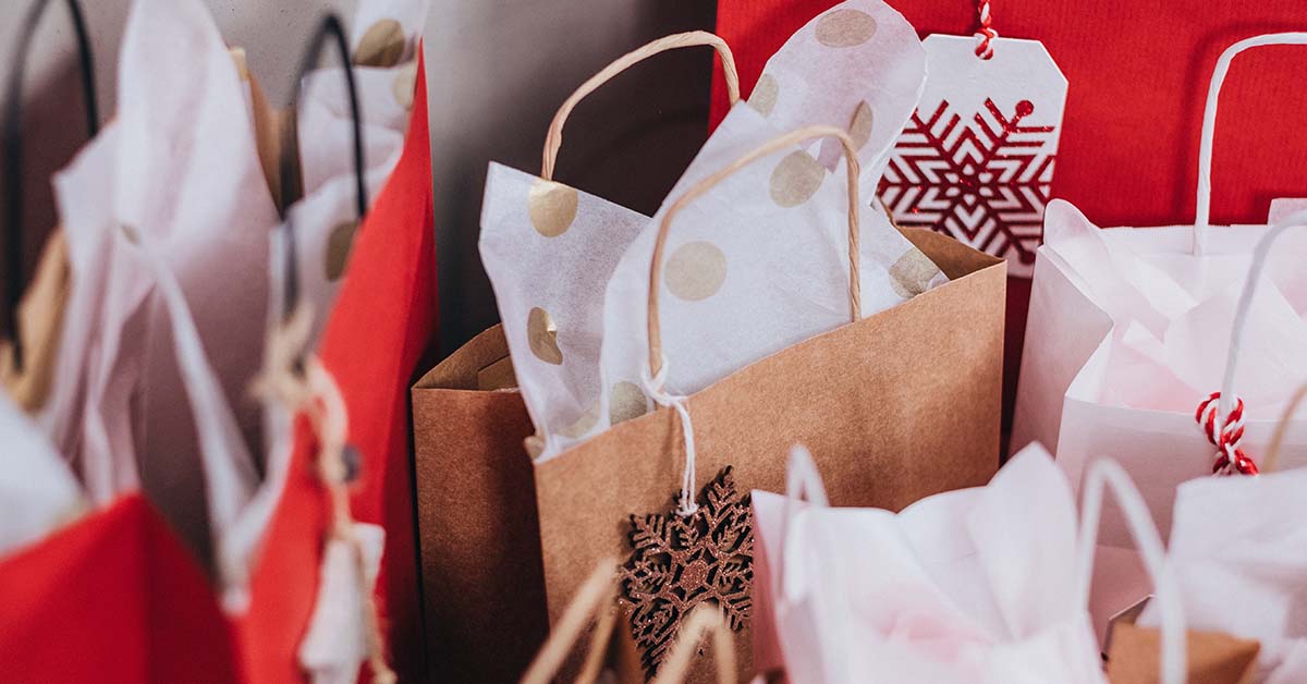 TQS takes on shopping local. IMAGE: a close-up shot of holiday gift bags (red, brown, snowflakes, and gold polka dots)