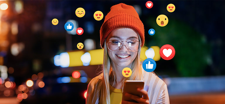 Girl smiling while looking at her phone. Emojis of people liking a video surrounding her.
